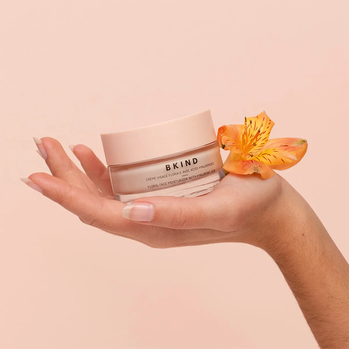 Crème visage florale BKIND tenue dans la paume, avec une fleur.